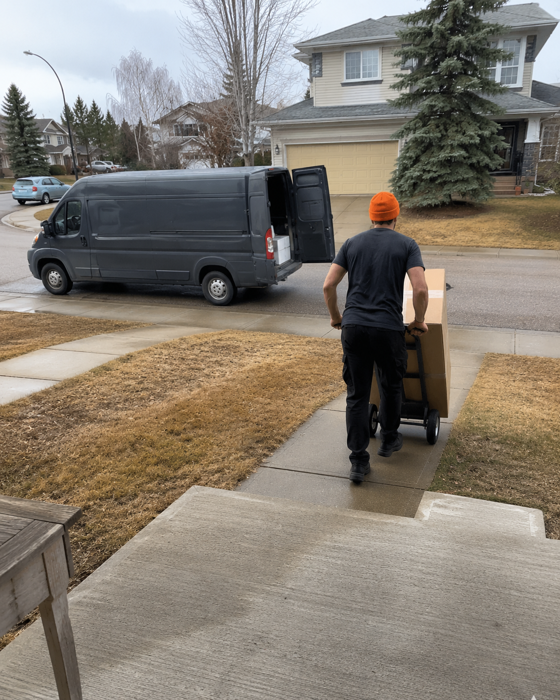 Mover wheeling a large boxed delivery up a front walk from the open cargo van at the curb